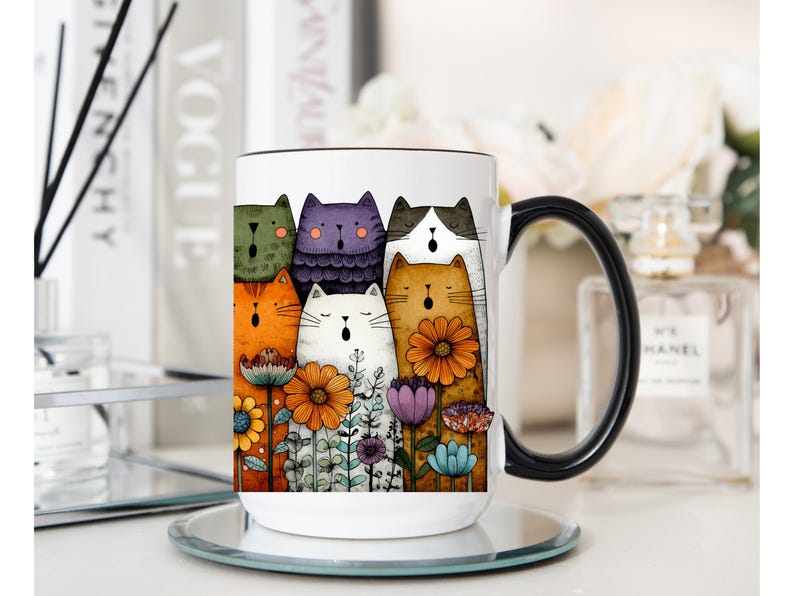May include: White ceramic mug with a black handle featuring a colorful illustration of singing cats and flowers. The cats are in various colors, including orange, purple, and green. The flowers are orange, purple, and blue.