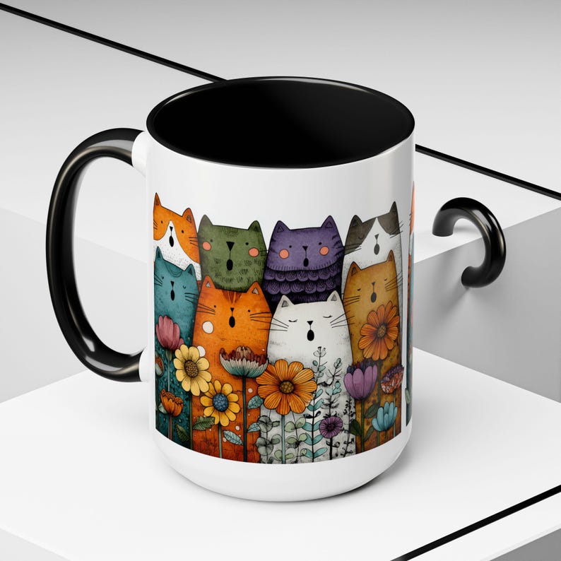 May include: White ceramic mug with a black interior and handle. The mug features a colorful illustration of cartoon cats and flowers. The cats are various colors, including orange, green, and purple. The flowers are yellow, orange, and purple.