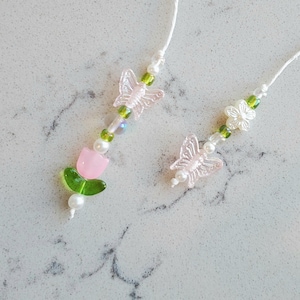 May include: Two beaded necklaces with pink butterfly charms, green leaves, and white flowers. One necklace has a pink tulip charm.