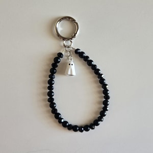 May include: A black beaded bracelet with a small white ghost charm. The bracelet is attached to a silver-colored clasp. The beads are faceted and reflect light. A cute Halloween-themed accessory.