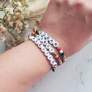 May include: Four beaded bracelets with the words "Sudan", "Congo", "Palestine", and "Palestine" spelled out on them. The bracelets are made with colorful beads and white letter beads.