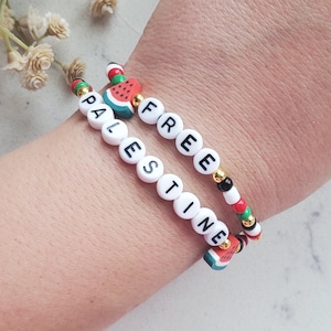 May include: Two beaded bracelets with the words "PALESTINE" and "FREE" spelled out in black letters on white beads. The bracelets are decorated with red, green, and white beads, and watermelon charms.
