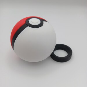 May include: A white, red, and black Pok&eacute; Ball with a separate black ring. The ball is round with a white center, a red top, and a black band separating the colors. The black ring is circular.