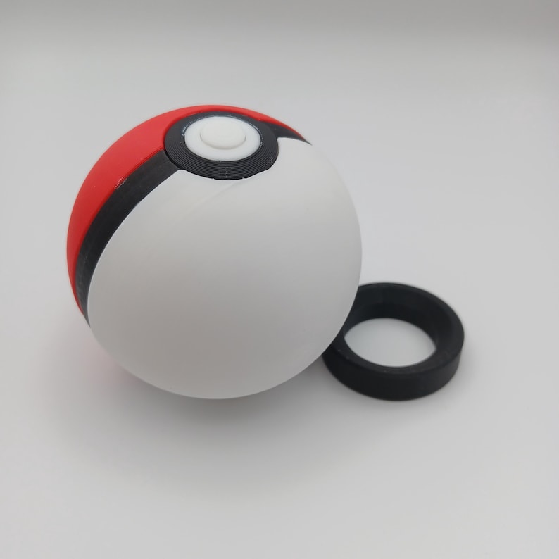 May include: A white, red, and black Pok&eacute; Ball with a separate black ring. The ball is round with a white center, a red top, and a black band separating the colors. The black ring is circular.