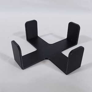 May include: Black plastic stand with four upright sides forming a square shape. The stand is designed to hold items in place.