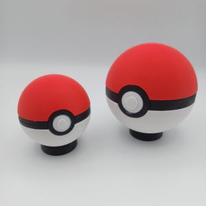 May include: Two red, white, and black Pok&eacute; Ball replicas. The top half is red, the bottom half is white, and a black band encircles the middle. A white circle is centered on the black band. The balls have a black base.