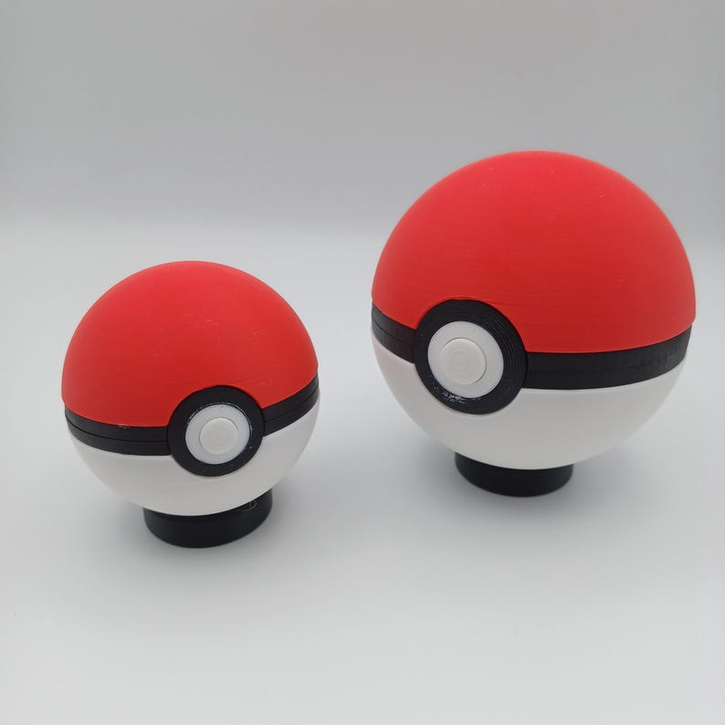 May include: Two red, white, and black Pok&eacute; Ball replicas. The top half is red, the bottom half is white, and a black band encircles the middle. A white circle is centered on the black band. The balls have a black base.