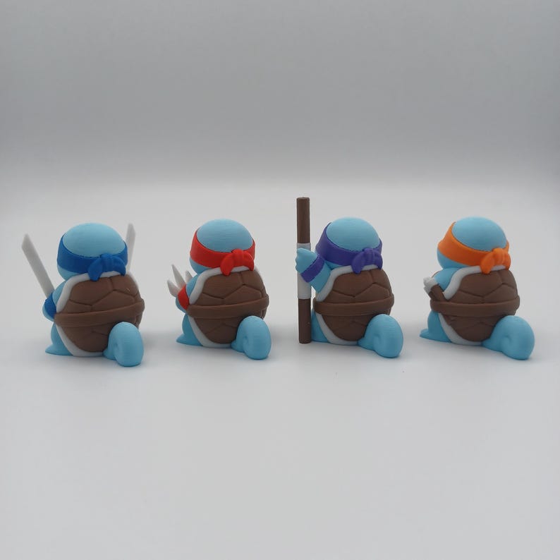 May include: Four blue turtle figurines with different coloured bandanas and weapons. The turtles are in a row, facing the right side of the image. The turtle on the left is holding two swords, the next turtle is holding two katanas, the third turtle is holding a staff, and the last turtle is holding a sai.