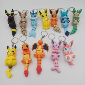May include: A collection of colorful character keychains featuring various designs. The keychains are made of plastic and have a metal ring for attaching to keys or bags. The characters include a yellow Pikachu, orange Charmander, and others.
