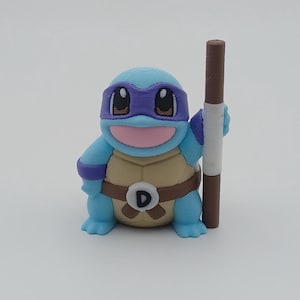 May include: A blue and purple 3D printed figurine of a turtle wearing a purple bandana and holding a brown stick. The turtle has a brown belt with a white "D" on it.