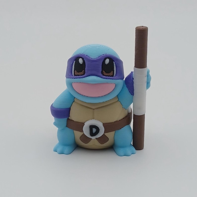May include: A blue and purple 3D printed figurine of a turtle wearing a purple bandana and holding a brown stick. The turtle has a brown belt with a white "D" on it.