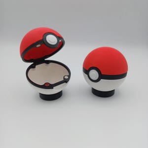 May include: Two red, white, and black novelty items resembling a Pok&eacute; Ball. One is open, revealing a white interior. The other is closed. Both have a black base and a white circle with a black outline.