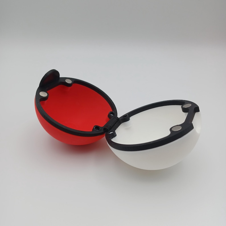 May include: An open, two-part, red and white sphere with a black border and hinge. The interior of one half is red, while the other is white. The sphere is designed with a black hinge and magnetic closures.