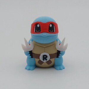 May include: A blue and white 3D printed Squirtle figurine wearing a red bandana with a black 'R' on its chest.