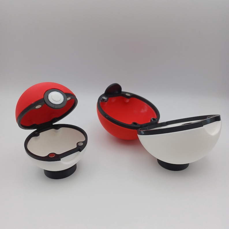 May include: Three open, red and white novelty containers, resembling a Pokeball. The containers are red on top and white on the bottom, with a black rim and a black base. One is open, revealing a white interior.