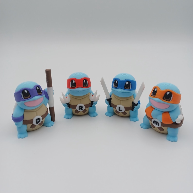 May include: Four small blue turtle figurines with different coloured masks and accessories. The turtles are wearing the letters D, R, L, and M on their shells.