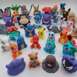 May include: A collection of various small, colorful plastic character figurines featuring diverse shapes, including creatures with wings, horns, and floral elements, arranged together on a plain white surface with no other objects present.