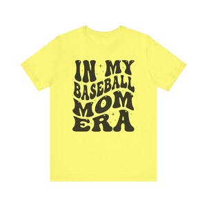 May include: Yellow t-shirt with black text that reads "In My Baseball Mom Era" in a retro font.