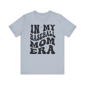 May include: Light blue t-shirt with black text that reads "In My Baseball Mom Era" in a retro font.