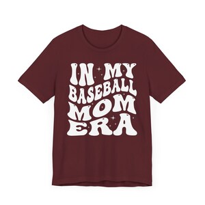 May include: Burgundy t-shirt with white text that reads "In My Baseball Mom Era" in a retro font.