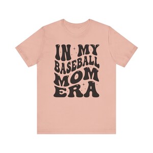 May include: A pink t-shirt with the text "IN MY BASEBALL MOM ERA" in black, retro-style lettering.