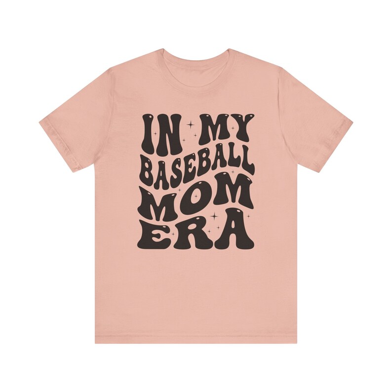 May include: A pink t-shirt with the text "IN MY BASEBALL MOM ERA" in black, retro-style lettering.