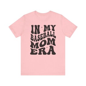 May include: Pink t-shirt with black text that reads "In My Baseball Mom Era" in a retro font.