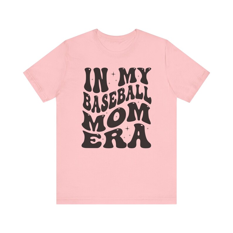 May include: Pink t-shirt with black text that reads "In My Baseball Mom Era" in a retro font.