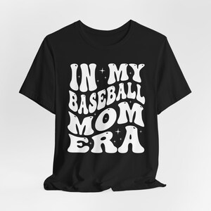 May include: Black t-shirt with white text that reads "In My Baseball Mom Era" in a retro font.