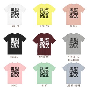 May include: Nine t-shirts in different colours featuring the text "In My Baseball Mom Era" in a retro font.