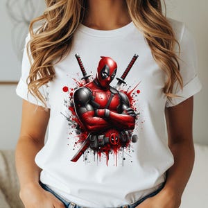 May include: White t-shirt with a Deadpool graphic. The design shows Deadpool in a red and black suit, with two katanas behind him. Red paint splatter effects add to the action-packed theme of the design.