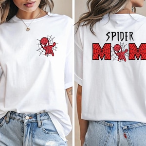 May include: White t-shirt featuring a red and black Spider-Man graphic on the front and back. The front graphic shows Spider-Man on a web. The back of the shirt says "SPIDER MOM" with a web design.