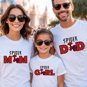 May include: Three people wearing white t-shirts with Spider-Man themed designs. The shirts read "Spider Mom", "Spider Dad", and "Spider Girl" in red and black lettering, with a Spider-Man graphic. All are wearing sunglasses.