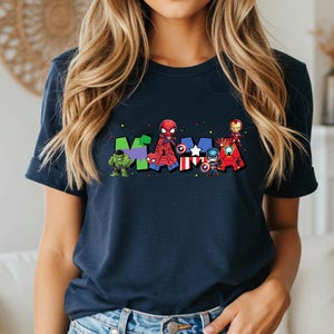 May include: Navy blue t-shirt featuring the word "MAMA" in colorful letters, each letter adorned with superhero characters. The Hulk, Spider-Man, Captain America, Iron Man, and other heroes are depicted.