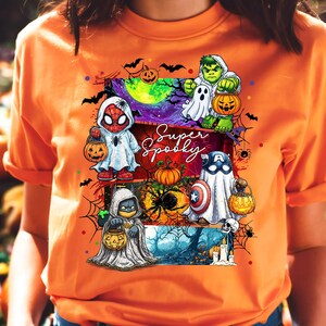 May include: Orange t-shirt featuring a Halloween-themed graphic. The design includes cartoon characters dressed as superheroes, holding jack-o'-lanterns, and the words "Super Spooky". The artwork incorporates bats, spiders, and a spooky night scene.