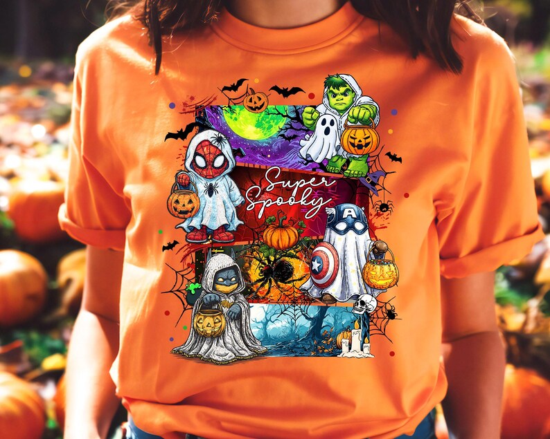 May include: Orange t-shirt featuring a Halloween-themed graphic. The design includes cartoon characters dressed as superheroes, holding jack-o'-lanterns, and the words "Super Spooky". The artwork incorporates bats, spiders, and a spooky night scene.