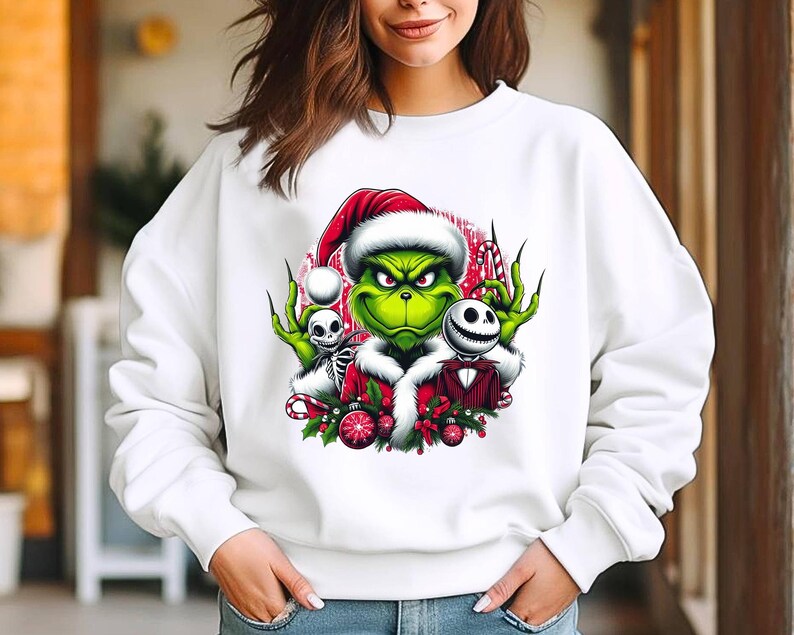 May include: White sweatshirt featuring a graphic of the Grinch wearing a Santa hat, with Jack Skellington and a skeleton. The Grinch is green with a red and white Santa hat. The graphic includes candy canes and Christmas ornaments.