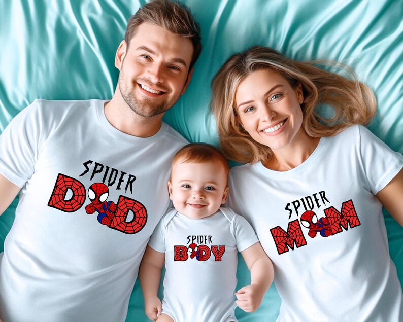 May include: White t-shirts and a onesie with a Spider-Man theme. The shirts say "Spider Dad", "Spider Mom", and "Spider Boy" in black text with a red web design and a Spider-Man graphic. Family matching apparel.