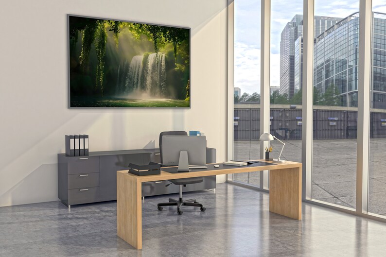 May include: A modern office with a large desk made of light wood. The desk has a black leather top and a black office chair. There is a large window behind the desk with a view of a city skyline. A framed picture of a waterfall in a lush green forest hangs on the wall.