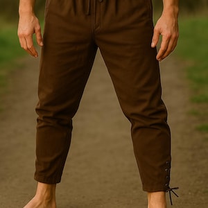 May include: Brown pants with a drawstring waist and ankle ties. The pants are a solid color and appear to be made of a soft fabric. The person is wearing a green shirt.