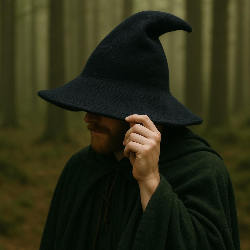 May include: A black witch hat with a wide brim and a pointed top. The hat is made of a textured fabric. The person in the image is wearing a dark green cloak.