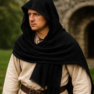 May include: A person wearing a black hooded cloak and a tan tunic, with a brown belt. The person is standing outdoors, with a stone archway in the background. The cloak is draped over the shoulders.