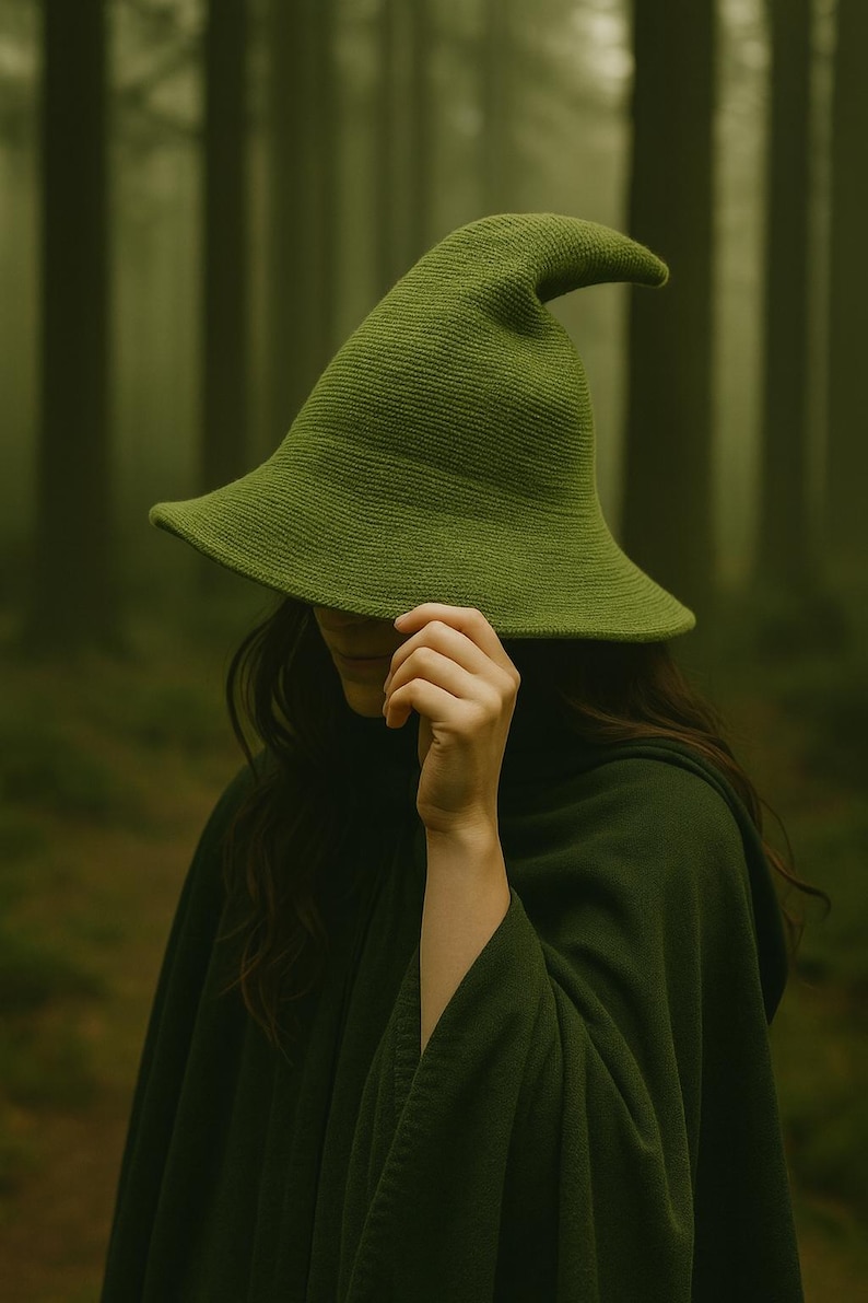 May include: A green witch hat with a wide brim and a pointed tip. The hat is made of a textured fabric and is worn with a matching green cloak. The background is a blurred forest scene.