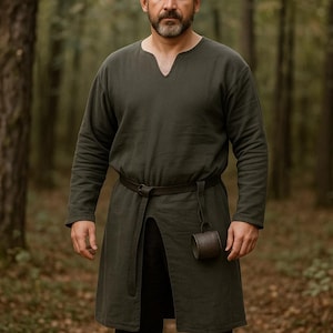 May include: A dark green tunic with long sleeves and a V-neck, worn with a brown belt and a small, cylindrical pouch. The tunic has a split front and is made of a textured fabric. The outfit is suitable for historical reenactment or costume events.