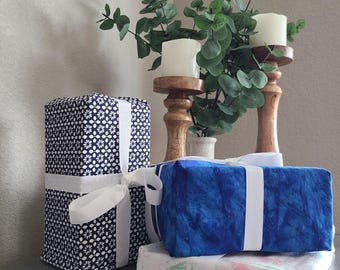 May include: Three wrapped gifts with white ribbon on a table. The gifts are wrapped in blue and white patterned paper. The gifts are in front of a wooden candle holder with white candles.