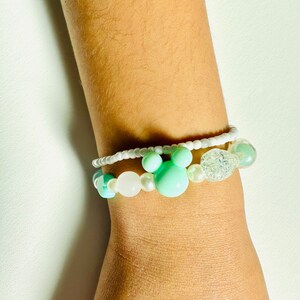 May include: A white and light green beaded bracelet with a white and silver charm. The bracelet has a Mickey Mouse head charm.