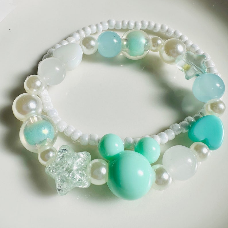 May include: A white and light blue beaded bracelet with a heart, star, and paw print charm. The bracelet is made with small white beads and larger light blue beads.