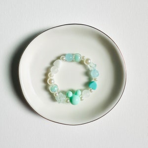 May include: A light blue and white beaded bracelet with a turquoise heart charm and a light blue Mickey Mouse charm.