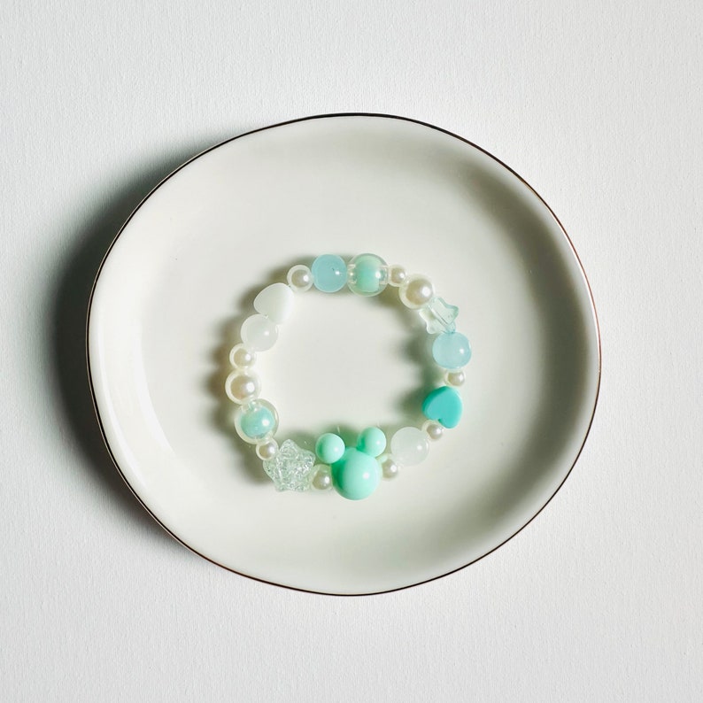 May include: A light blue and white beaded bracelet with a turquoise heart charm and a light blue Mickey Mouse charm.