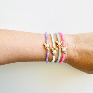 May include: Five beaded bracelets with a pearl and gold bear charm. The bracelets are in shades of purple, white, light blue, and pink.